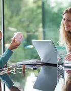 Mother and daughter sitting at table, counting coins from a piggy bank